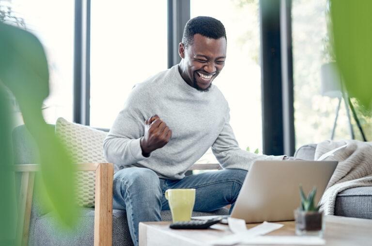 Man celebrating being debt-free while going over paperwork and using a laptop