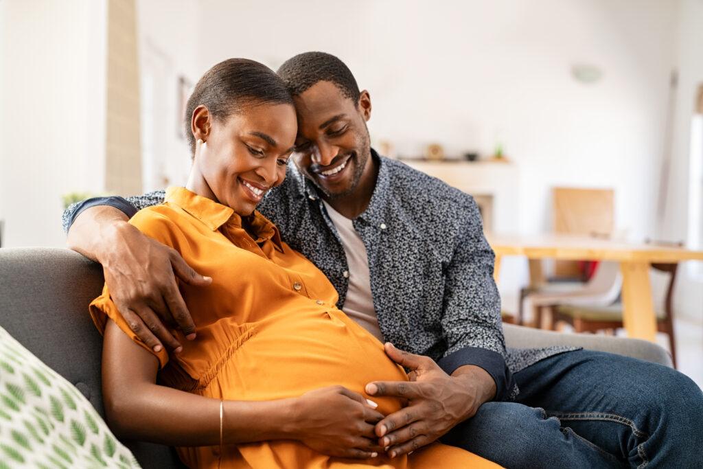 Black expectant parents sitting on sofa 
